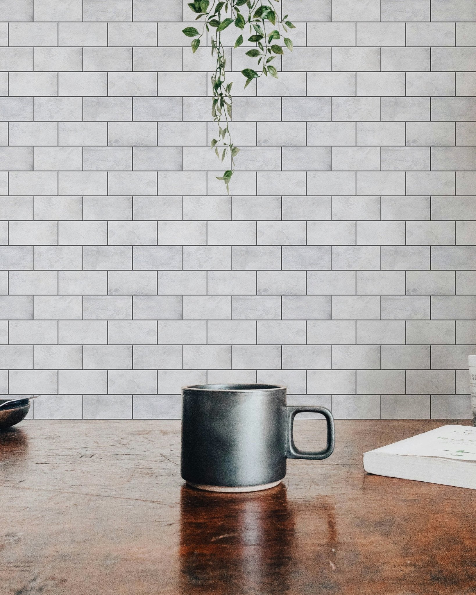 Coffee mug on a wooden table with hanging ivy and brick wallpaper.