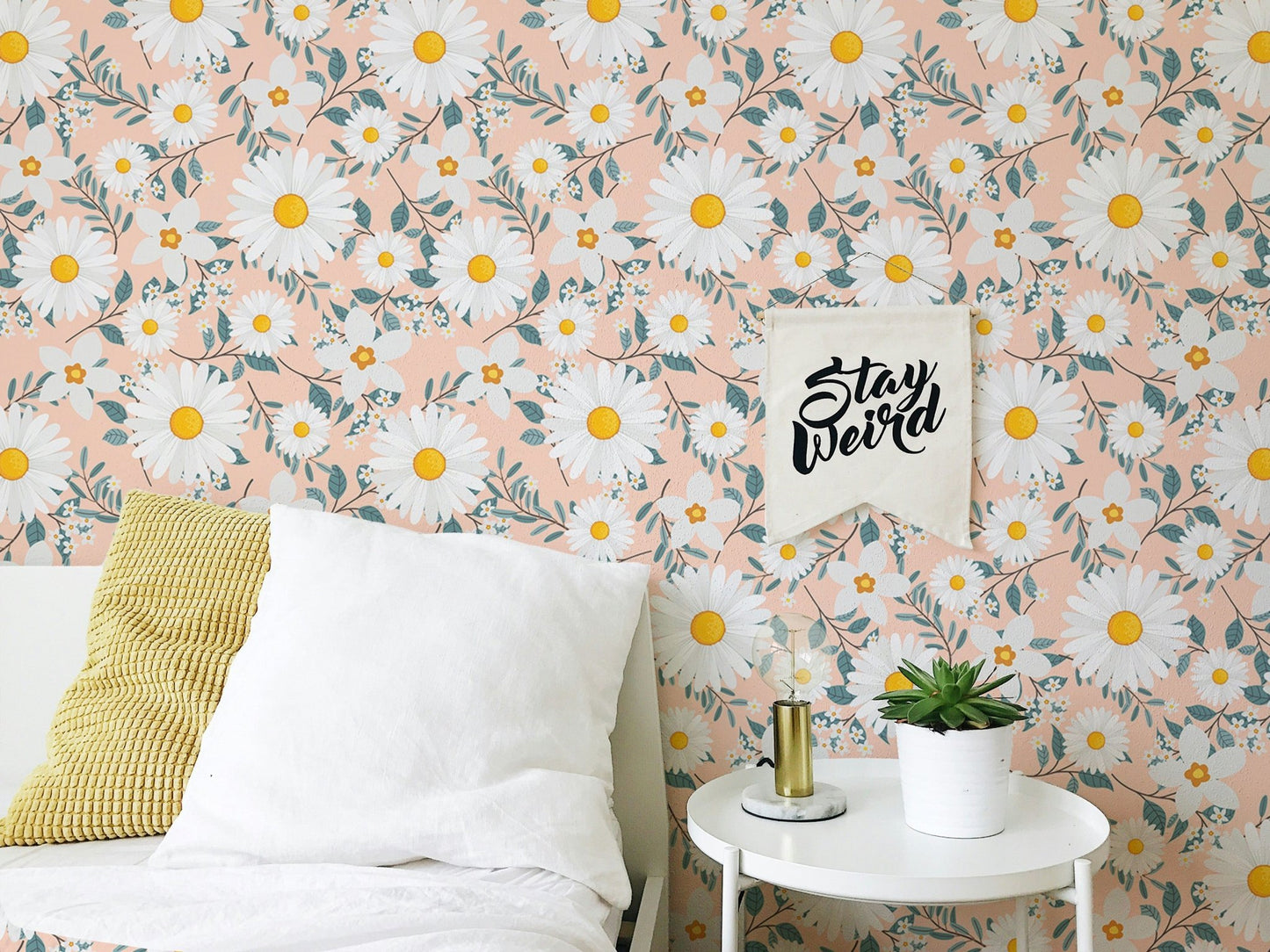Daisy patterned wallpaper behind a white bed with yellow and white pillows.