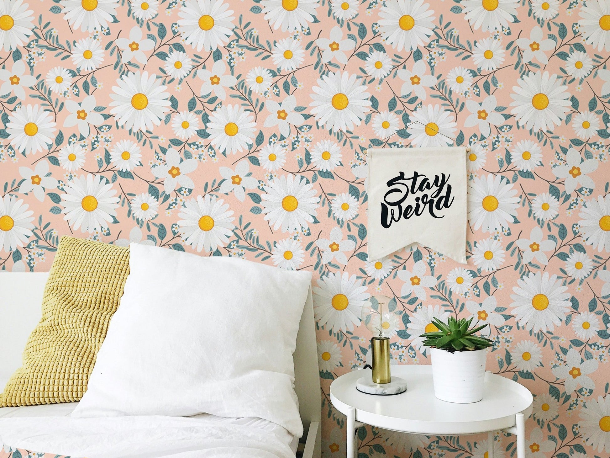 Daisy patterned wallpaper behind a white bed with yellow and white pillows.