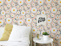 Daisy patterned wallpaper behind a white bed with yellow and white pillows.