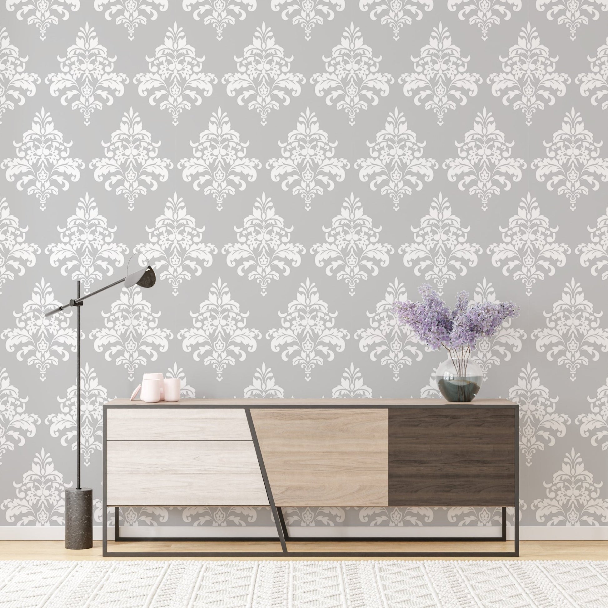 Symmetrical grey damask pattern wallpaper behind a modern sideboard and floor lamp.