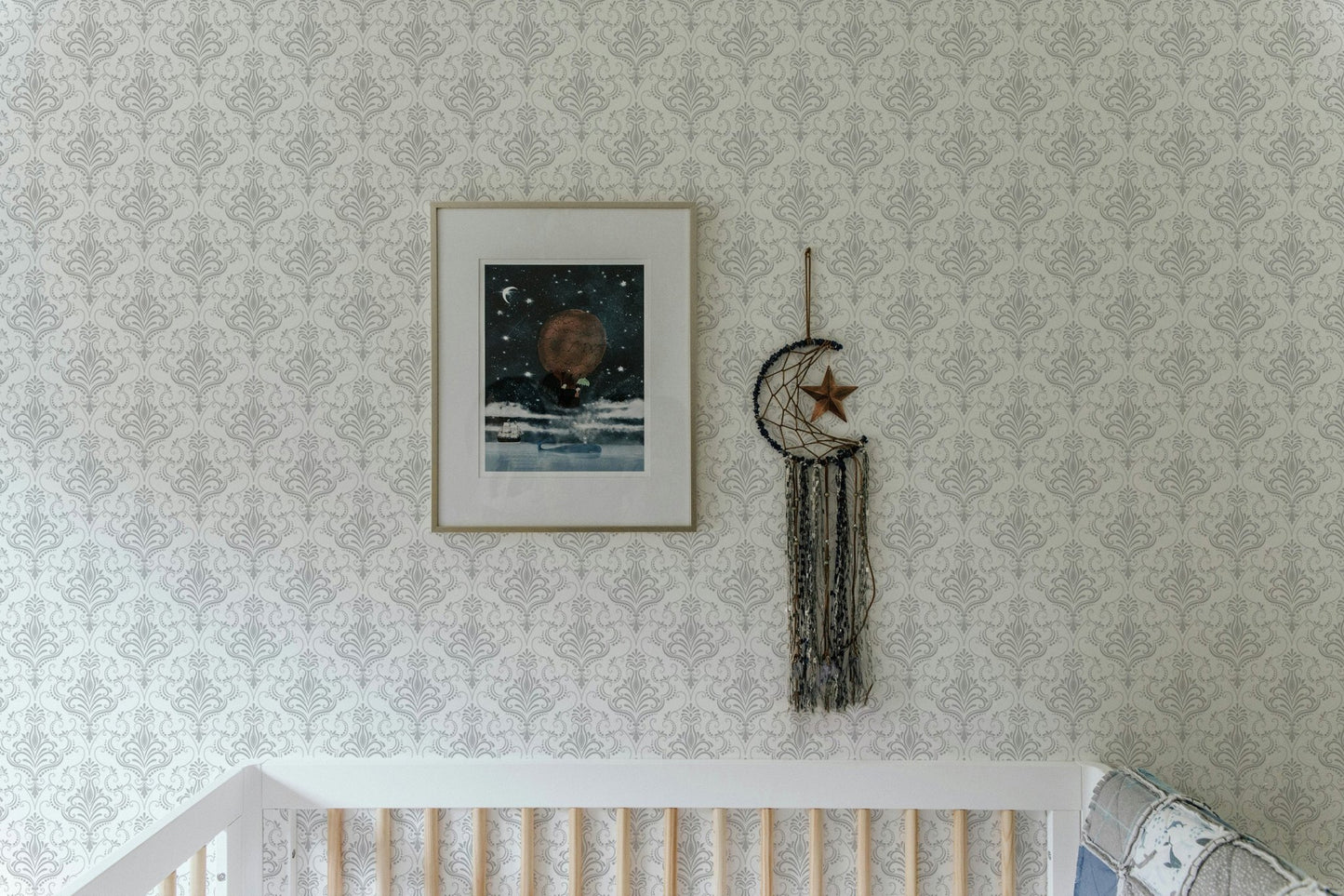 Damask wallpaper in a nursery room above a wooden crib with framed art.