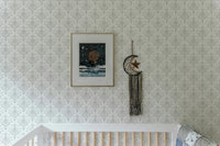 Damask wallpaper in a nursery room above a wooden crib with framed art.